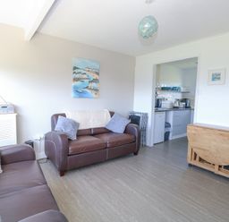 A living room with two brown sofas and a wooden folding table next to an open kitchen at Chalet 38 in Hemsby