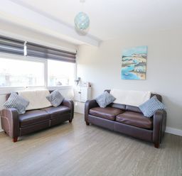 A living room with two brown leather sofas with cushions and a window with blinds at Chalet 39 in Hemsby