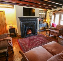 A living room with wooden beams a fireplace sofa armchairs a red rug and a window seat at Pagecroft Cottage in Haydon Bridge