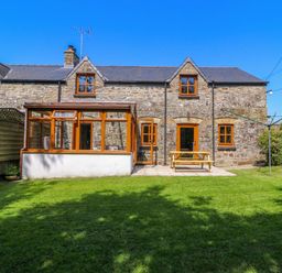 A stone house with wooden framed windows and a conservatory overlooking a grass garden at Cove Cottage in Llangrannog