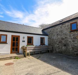 An exterior courtyard with stone and white walls wooden windows and a wooden bench at Cove Cottage in Llangrannog