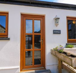 Cottage exterior with wooden door and two windows and a planter with flowers at Cove Cottage in Llangrannog