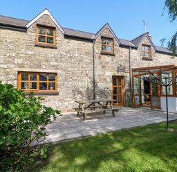 A stone house with wooden windows a patio table and a grassy garden at Y Bwthyn in Llangrannog