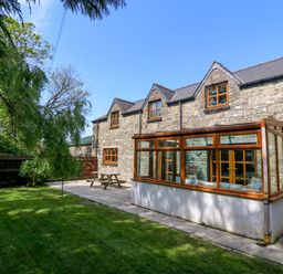 A stone house with a glass conservatory and wooden picnic table in a garden at Y Bwthyn in Llangrannog