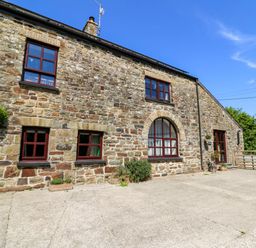 Stone exterior of a house with multiple windows and a paved area in front at Coach House in Llangrannog