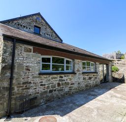 Stone exterior of a building with windows and a wooden staircase leading to an upper area at Coach House in Llangrannog
