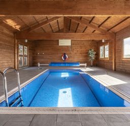 An indoor swimming pool with a ladder and seating area at Coach House Llangrannog