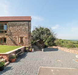 The exterior of a stone building with windows and a gravel driveway with flower pots and a bench at Newlands Barn in Wellington