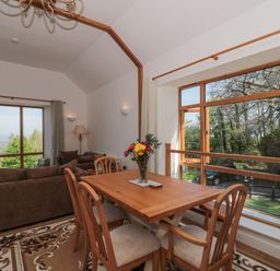 A dining table with chairs and a vase of flowers next to large windows and a seating area with sofas in a room at Newlands Barn in Wellington
