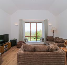 A living room with brown sofas a wooden table a television and a large window at Newlands Barn in Wellington