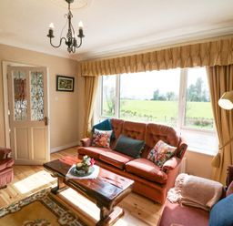 A sitting room with sofa chairs a wooden coffee table and large window with curtains at Teach Ards in Kilgarvan County Kerry