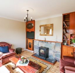 A living room with upholstered armchairs a wooden coffee table a stone fireplace with an electric stove and built in wooden shelves at Teach Ards Kilgarvan County Kerry