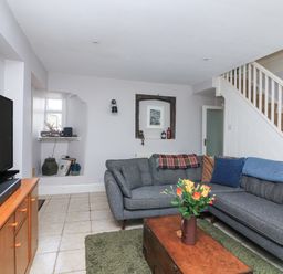 A living room with gray sectional sofa a wooden coffee table with flowers a television on a wooden stand and stairs at Joymead in Malborough
