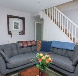 A living room with a grey sofa, throws and cushions, a wooden coffee table with flowers, stairs and a recessed wall shelf at Joymead in Malborough