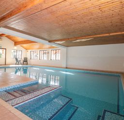 An indoor swimming pool with steps leading into the water and two chairs near windows at Beaver Cottage in Little Thirkleby near Thirsk