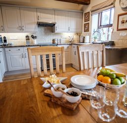 A kitchen with white cabinets wooden dining table with fruit bowl plates and wine glasses at Beaver Cottage in Little Thirkleby near Thirsk
