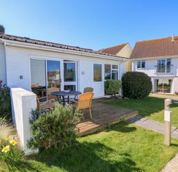 A patio with a round table and four chairs outside a white house with sliding glass doors and garden plants at Cape A9 Norton Near Freshwater