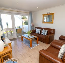 A living room with two brown leather sofas a wooden coffee table and glass doors leading to an outdoor seating area at Cape A9 Norton Near Freshwater