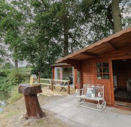 A cabin with wooden deck and bench at Carps Well Lodge Hatton near Shrewley