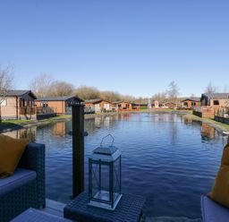 An outdoor seating area with yellow pillows overlooking a pond surrounded by wooden cabins at Coniston View Lodge in Warton near Carnforth