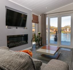 A living room with a wall-mounted tv and electric fireplace glass doors with curtains and a coffee table at Coniston View Lodge in Warton near Carnforth