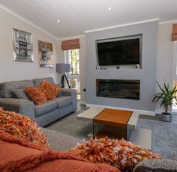 A living room with grey sofas and orange cushions a coffee table a wall-mounted television and a fireplace at Coniston View Lodge in Warton near Carnforth