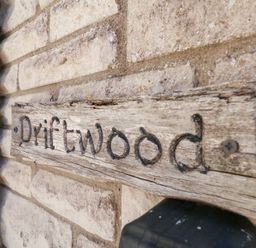A wooden sign that reads Driftwood on a brick wall at Driftwood in Weymouth