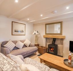 A living room with sofas cushions a wood burning stove a wooden coffee table and a television at Harbour View in Polperro