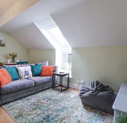 A living room with a grey sofa and colorful cushions a small table with a lamp a bean bag chair a rug a TV on a stand and a window in the ceiling at Cuddfan at Swallow Cottage in Rhydtalog near Coedpoeth