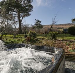 An outdoor hot tub with water jets in a garden with trees and hills in the background at White Haywood Farmhouse & Barn in Craswall
