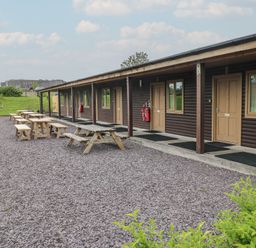 Outdoor area with wooden picnic tables and benches next to a building with multiple wooden doors and windows at Sycamore in Cowbridge