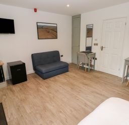 A room with a blue sofa a wall mounted TV a microwave and two desks with chairs at Sycamore in Cowbridge