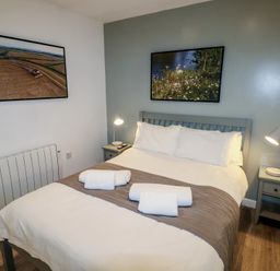 A bedroom with a double bed two bedside tables with lamps and framed pictures on the walls at Beech in Cowbridge