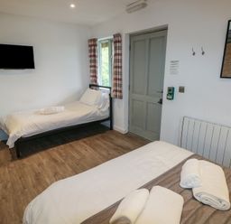 A room with two beds a wall-mounted TV a wooden floor and a door at Beech in Cowbridge