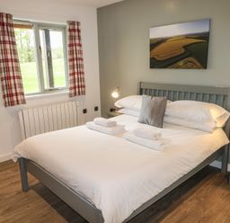 A bedroom with a double bed white bedding bedside tables and lamps a window with check curtains and a landscape picture on the wall at Alder in Cowbridge