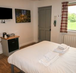 A bedroom with a bed towels a small fridge a television a picture on the wall and a window with curtain at Alder in Cowbridge