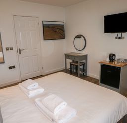 A bedroom with a bed towels a mirror a desk a chair a mini fridge a kettle and a wall-mounted television at Alder in Cowbridge