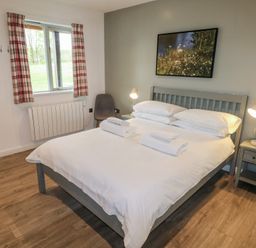 A bedroom with a bed with white linens two bedside tables with lamps a window with plaid curtains and a chair at Cherry in Cowbridge
