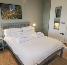 A bedroom with a gray bed frame and white bedding two bedside tables with lamps a wall mirror and a nature painting at Cherry in Cowbridge