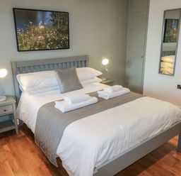 A bedroom with a double bed two bedside tables with lamps a mirror and a painting above the bed at Chestnut in Cowbridge