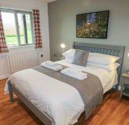 A bedroom with a bed made with white linens gray runner and pillows bedside tables with lamps and a window with red plaid curtains at Chestnut in Cowbridge