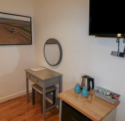A small room corner with a table and stool under a round wall mirror two blue mugs kettle and a container with coffee pods on a wooden surface below a wall mounted television at Chestnut in Cowbridge