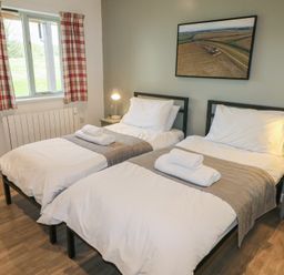 A bedroom with two single beds with white bedding and towels on them bedside tables with lamps and a window with plaid curtains at Oak in Cowbridge