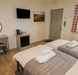 A bedroom with two single beds and towels on them a desk with mirror a television a kettle and a window with plaid curtains at Oak in Cowbridge