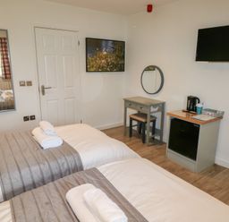 A bedroom with two beds with folded towels a wall-mounted television a small desk with a round mirror a mini fridge and a tea kettle at Oak in Cowbridge