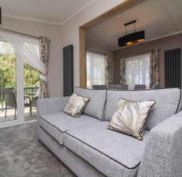 A living room with a grey sofa and patterned cushions next to glass doors leading to a balcony at 16 Manleigh Park in Combe Martin