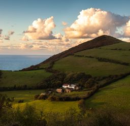 A scenic view of hills and a farmhouse near the ocean at 16 Manleigh Park in Combe Martin