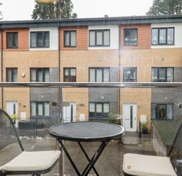 A balcony with a round metal table and two black chairs with white cushions overlooking modern townhouses at 13 Clock Tower Court in Charlestown