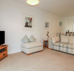 A living room with a striped sofa a TV on a wooden stand and two framed pictures on the wall at 13 Clock Tower Court in Charlestown