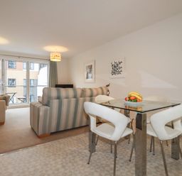A sitting room with a striped sofa a beige sofa a glass dining table with white chairs and a wall clock at 13 Clock Tower Court in Charlestown